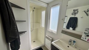 Ett badrum med en dusch som är avskärmad med glasväggar, ett handfat med toalettartiklar och en spegel med konst på väggen.
