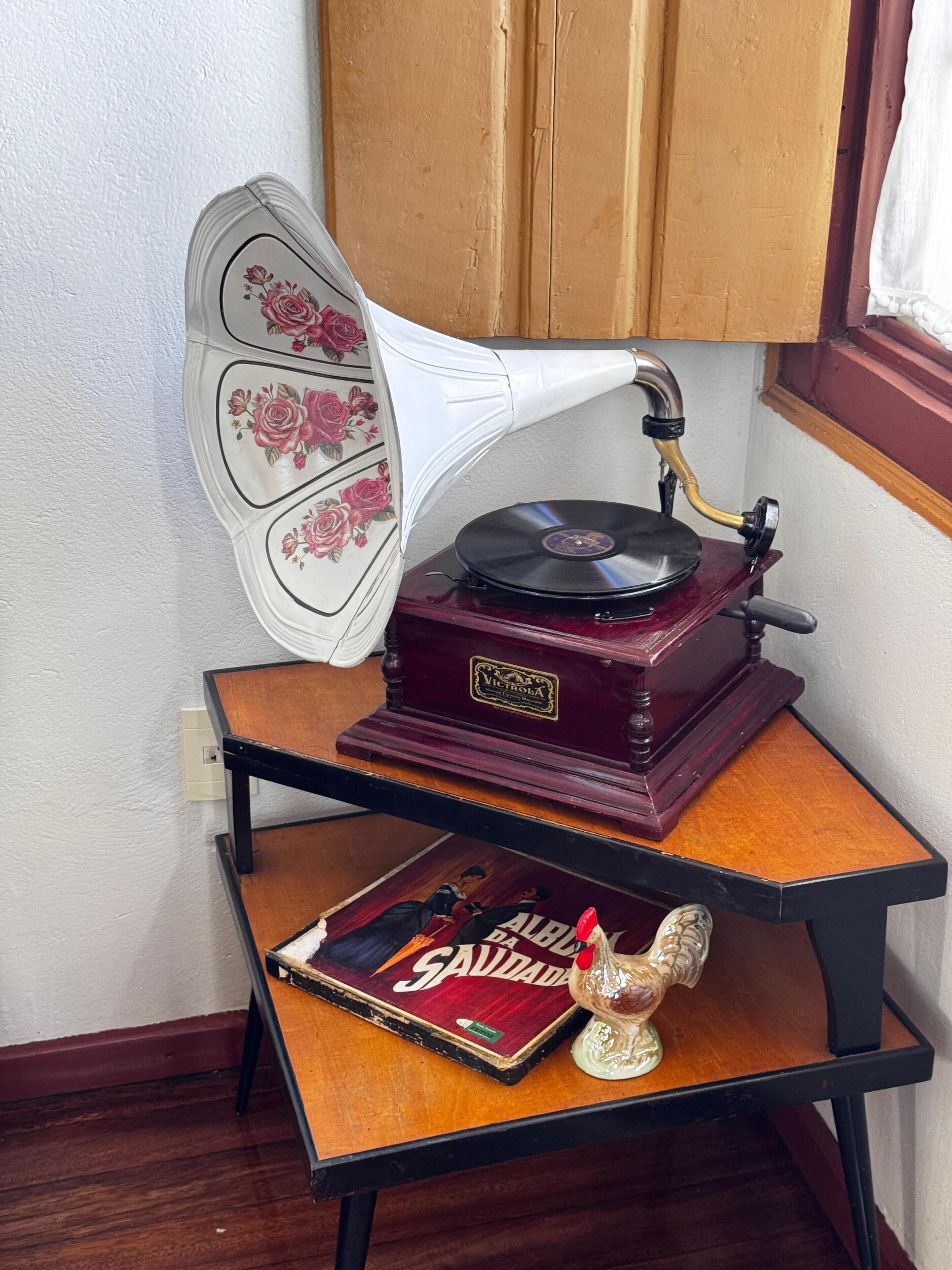 Tocadiscos Victrola antiguo sobre una mesa de madera con un altavoz estampado con motivos florales y un disco de vinilo titulado 'Saddam Hussein'.