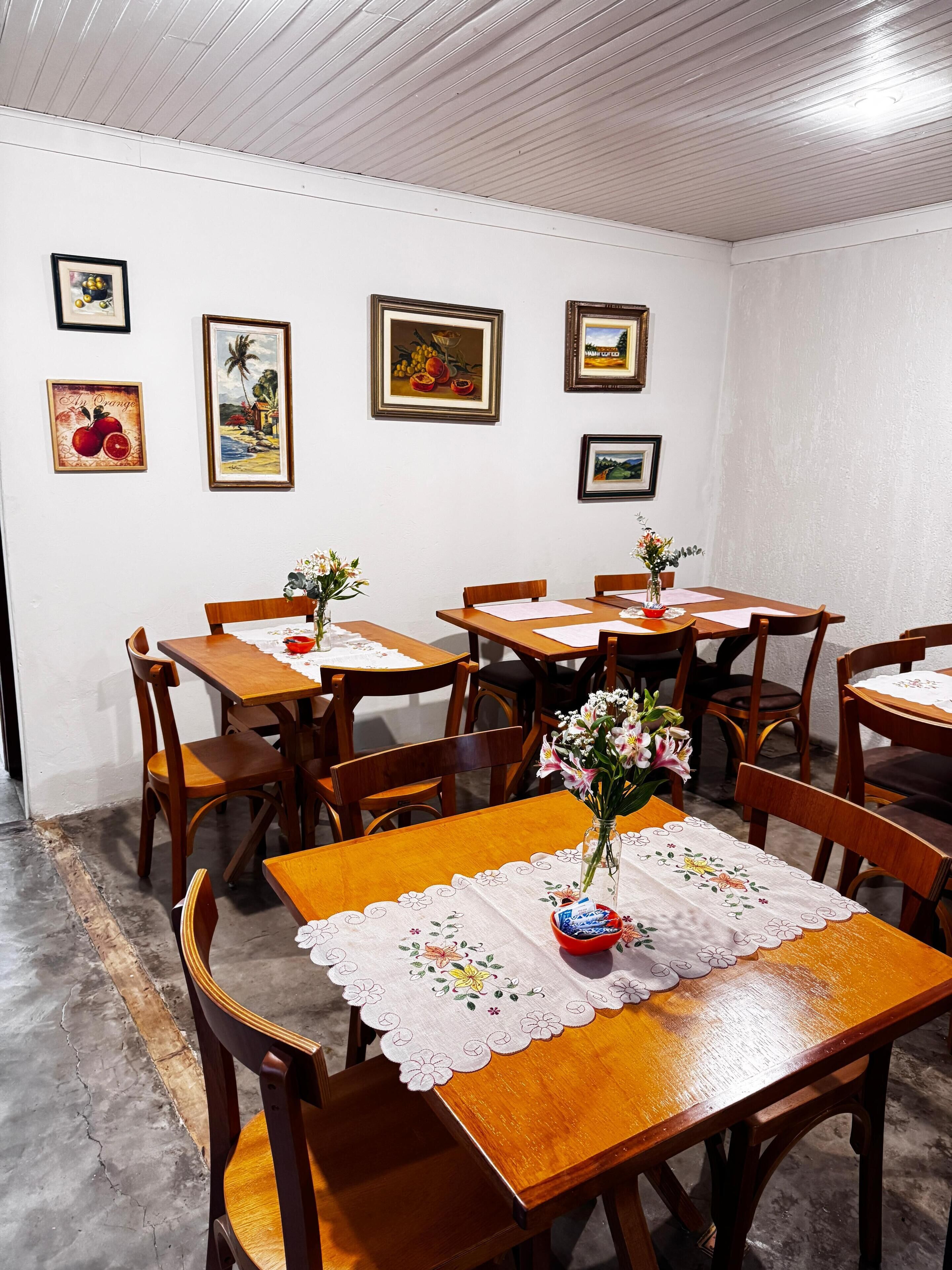 A dining area with wooden tables and chairs, floral tablecloths, and framed artwork on the walls.