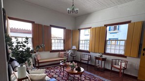 A spacious living room with a patterned rug, wooden furniture, and large windows with shutters.