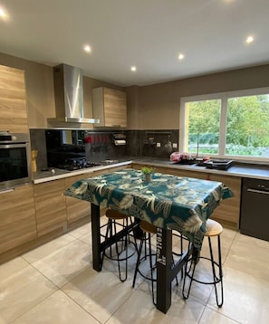 A modern kitchen with a central island, stainless steel appliances, and a window providing a view of greenery.