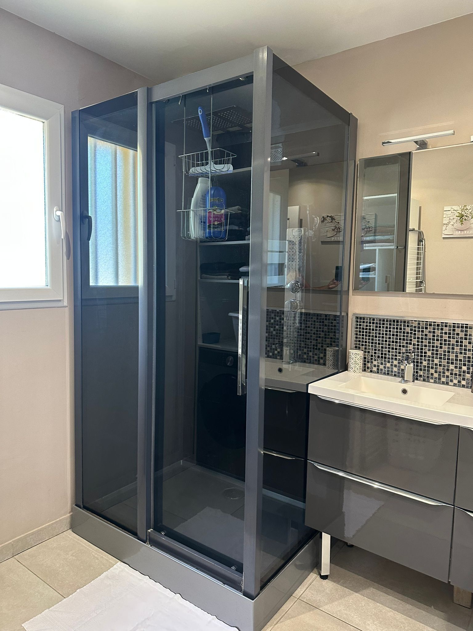 Une salle de bain moderne avec une douche à parois de verre, un lavabo blanc et un mur recouvert de carreaux.