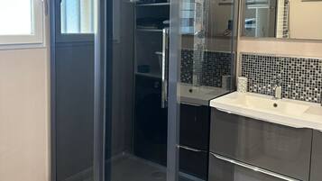 Une salle de bain moderne avec une douche à parois de verre, un lavabo blanc et un mur recouvert de carreaux.
