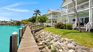 Un hôtel situé au bord de l’eau, doté d’une jetée en bois menant à une piscine, et entouré d’une végétation luxuriante et de palmiers.
