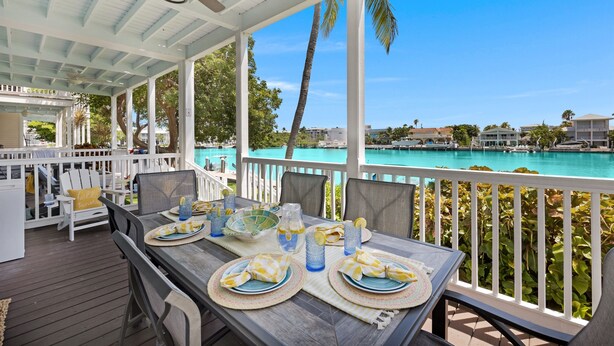 Un espace extérieur abrité, aménagé pour prendre les repas, avec vue sur une piscine turquoise et des palmiers.