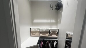 A narrow walk-in closet with shelves, hanging shoes, and a clothing rack.