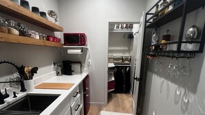 A narrow kitchen with a white sink, wooden shelves, and a white rug.
