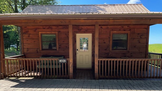 Une cabane en bois avec deux fenêtres, une porte et une véranda dotée d’un banc.