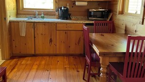 Une cuisine rustique aménagée dans une cabane en bois, avec un plan de travail en bois, un évier, une machine à café, un four à micro-ondes et une table à manger avec des chaises.