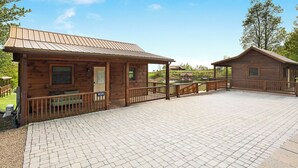 Une cabane en bois dotée d’un porche couvert et d’une terrasse dallée.