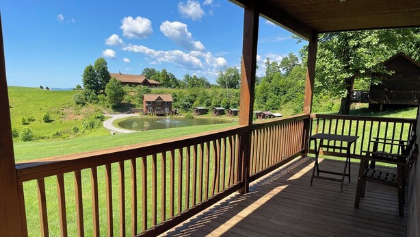 A wooden deck with a view of a pond, a house, and surrounding greenery. - Cabin #3 The Sky Retreat - Off the Blue Ridge Parkway (Purlear)