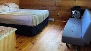 A wooden cabin room with a bed, a small sofa, a ceiling fan, an air conditioning unit, and a television. - Cabin #3 The Sky Retreat - Off the Blue Ridge Parkway (Purlear)