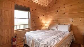 A wooden cabin bedroom with a bed, a window, a nightstand, and a fire extinguisher. - Cabin #4 The Sky Retreat - Off the Blue Ridge Parkway (Purlear)