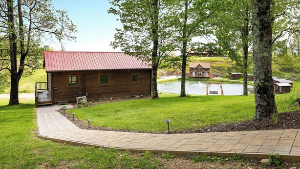 A wooden cabin with a red roof, a paved walkway, and a pond in the background. - Cabin #4 The Sky Retreat - Off the Blue Ridge Parkway (Purlear)