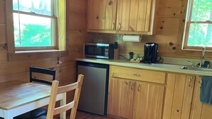 Eine Holzhütte mit einer Küche, einem Esstisch, Stühlen, einer Mikrowelle, einer Kaffeemaschine und einem Geschirrspüler.