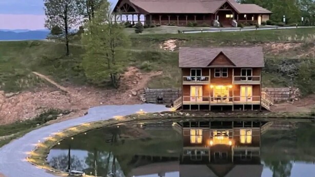 A two-story wooden house with a balcony, situated on a grassy hill with a pond in front. - Cabin #14 The Sky Retreat - Off the Blue Ridge Parkway (Purlear)