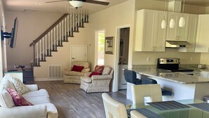 A spacious living area with a sofa, dining table, and chairs, a kitchen with modern appliances, and a staircase leading to another level. - Cabin #14 The Sky Retreat - Off the Blue Ridge Parkway (Purlear)
