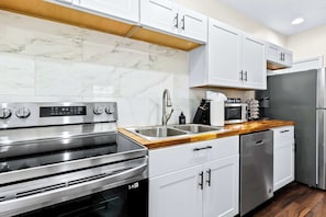 Una cocina moderna con armarios blancos, electrodomésticos de acero inoxidable y encimera de madera.