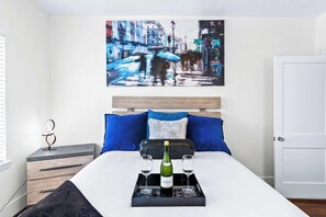 A hotel room with a bed, a bedside table, a wall-mounted artwork, and a tray with a bottle and glasses.