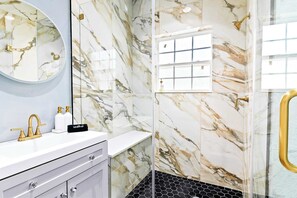 A bathroom with a marble wall, a round mirror, a gold faucet, and a black and white tiled floor.