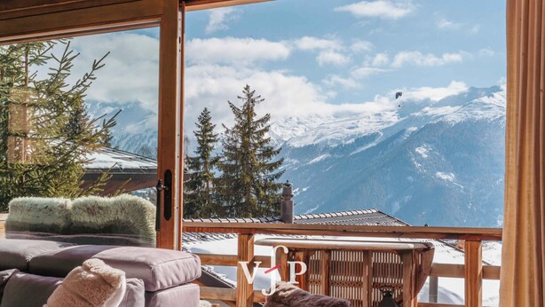 A room with a large window offering a mountain view, a wooden ceiling, and a cozy seating area with cushions.