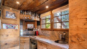 A wooden kitchen with a built-in oven, a sink, and a window with curtains.