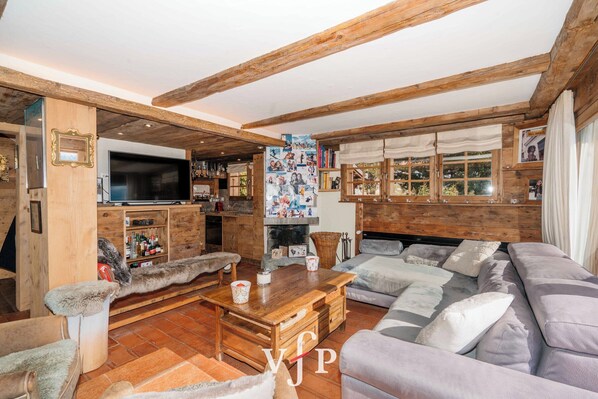 Una sala de estar acogedora con vigas de madera, un televisor de pantalla plana grande, una chimenea y un área de estar confortable.