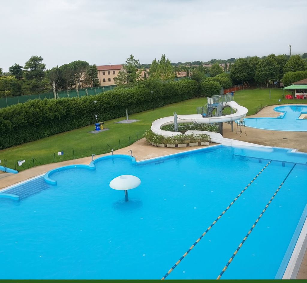A swimming pool with a water slide, surrounded by a green lawn and a fence.