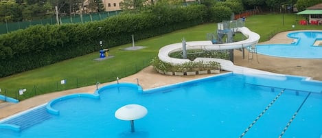A swimming pool with a water slide, surrounded by a green lawn and a fence.