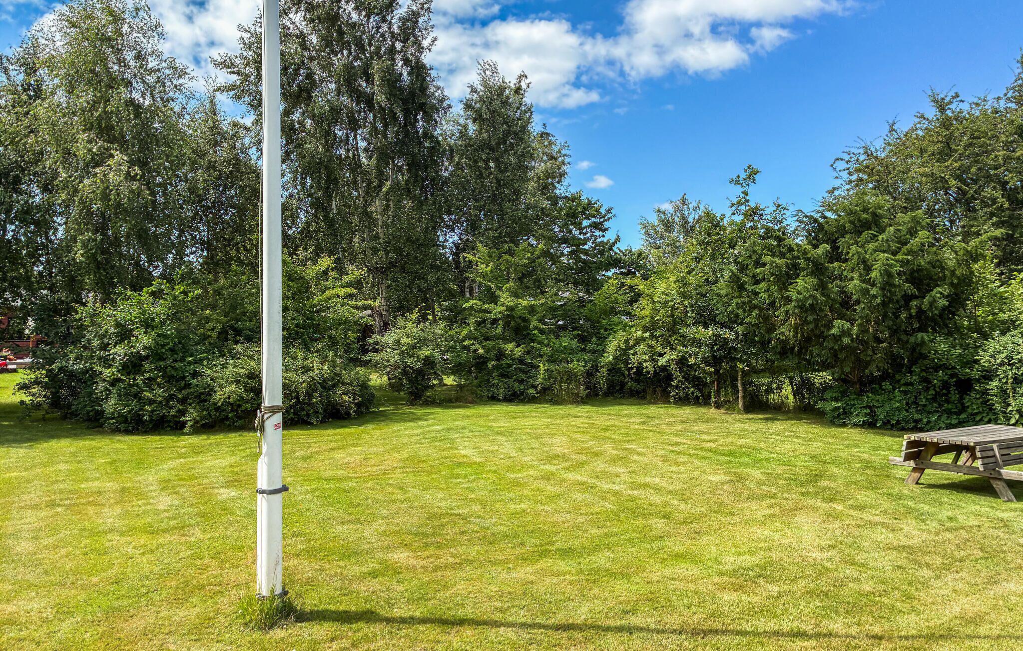 A grassy area with a tall pole, surrounded by dense trees and a picnic table.
