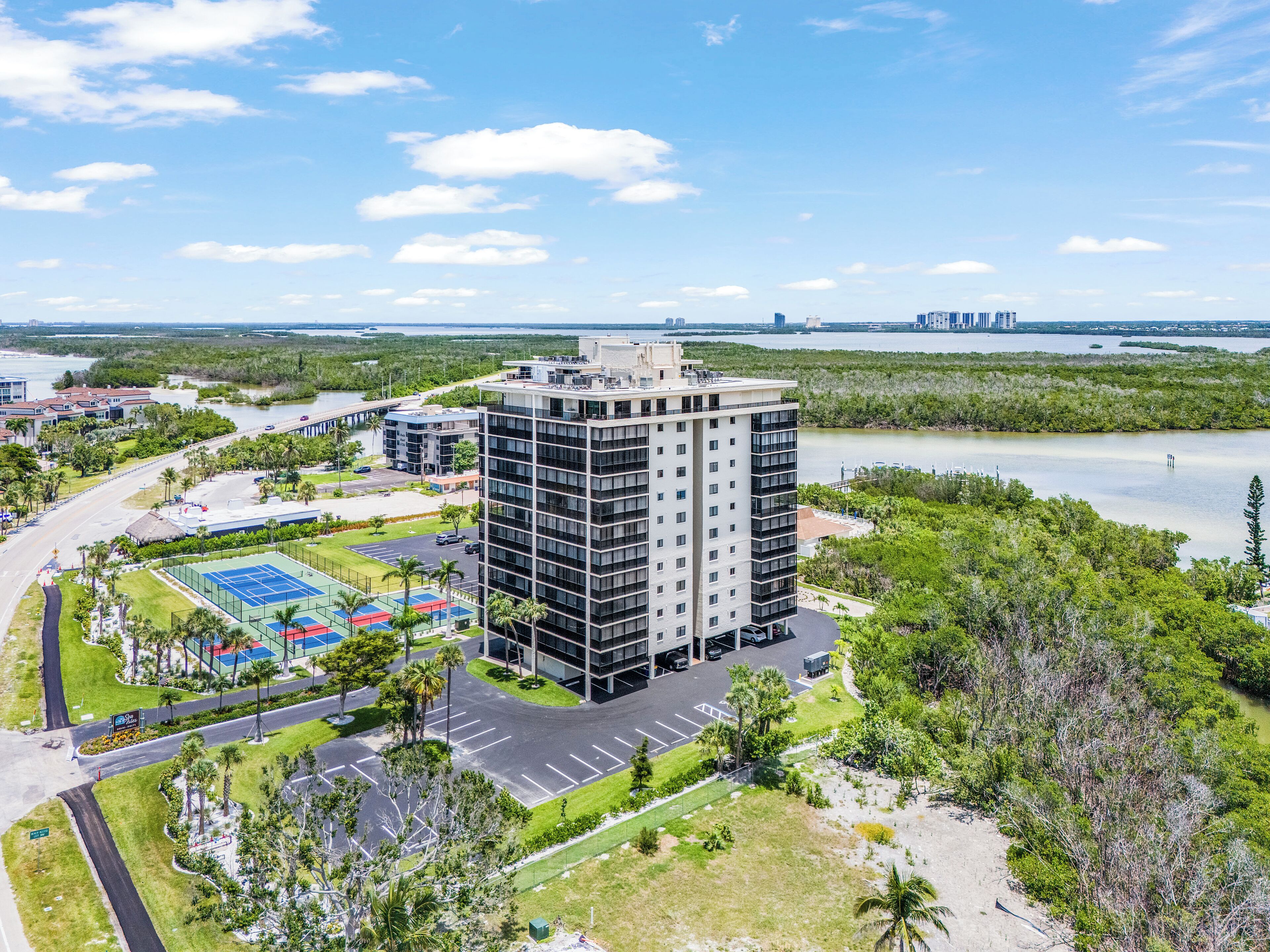 A high-rise hotel with multiple floors, a tennis court, and a parking area.