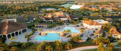 A resort with a large swimming pool, multiple buildings, and a golf course in the background.