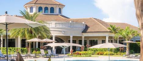 A resort with a swimming pool, lounge chairs, umbrellas, and a building with a tiled roof.