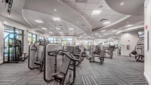 A modern gym with various exercise machines, large windows, and a patterned carpet. - Enjoy views of the immaculate green from your screened lanai at Lakeside National - Golfside Escape (Bradenton)