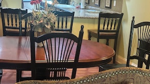 Un comedor con una mesa y sillas de madera, un jarrón con flores, y una cocina al fondo.