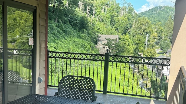Un balcón con una mesa y sillas, un ventilador de techo y vistas a un paisaje verde.