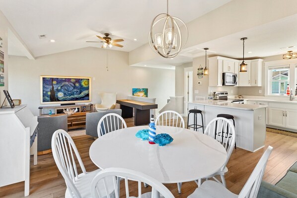 Una cocina moderna con armarios blancos, una isla central y un comedor con mesa y sillas blancas.