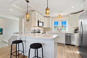 Una cocina moderna con armarios blancos, electrodomésticos de acero inoxidable y dos taburetes negros.