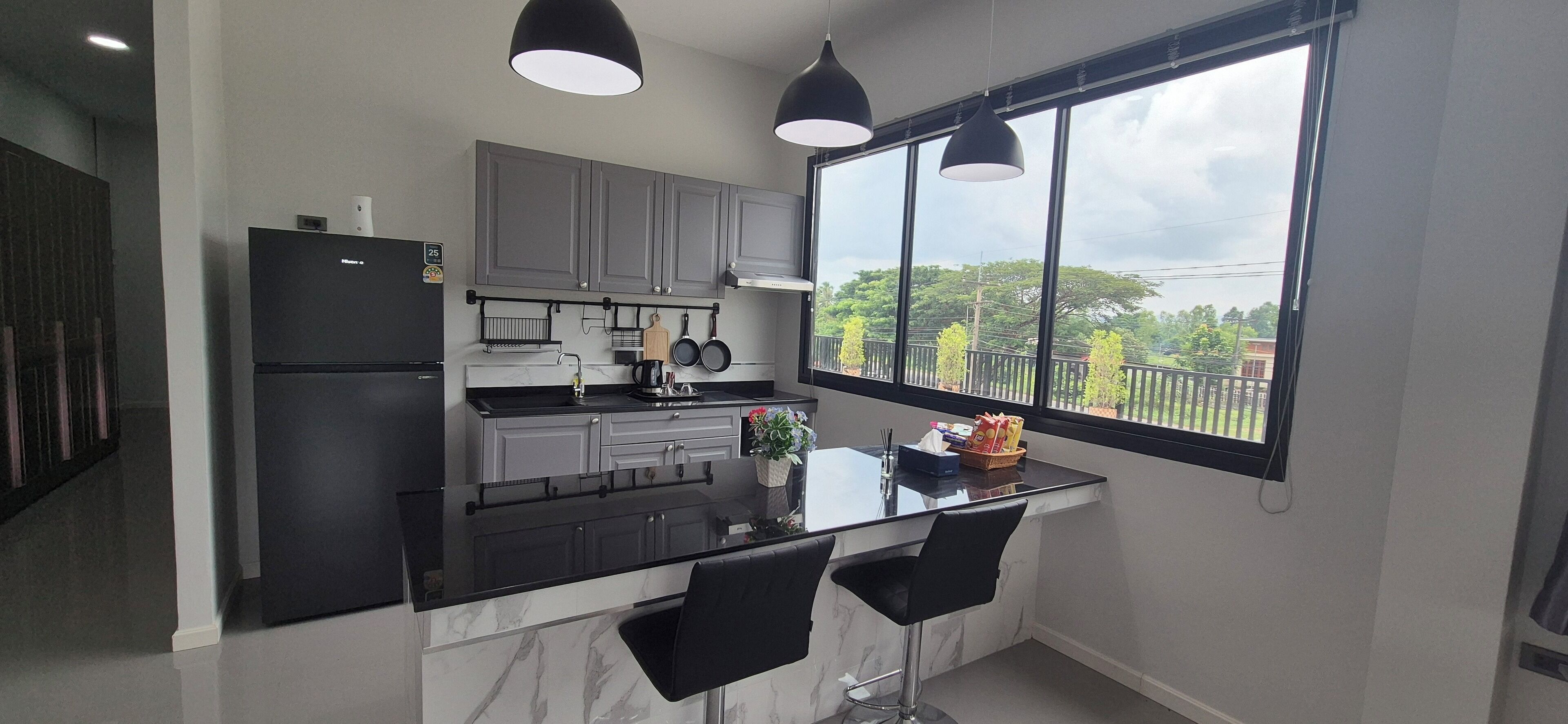 A modern kitchen with grey cabinets, a black countertop, and a window with a view of trees and buildings.