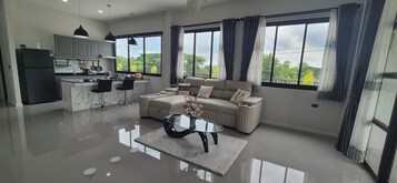 Uma sala de estar moderna com um sofá, uma mesa de centro de vidro e vista para o exterior.