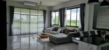 Uma sala de estar moderna com sofá, mesa de centro e mesa de jantar com cadeiras. Grandes janelas oferecem vista para o exterior.