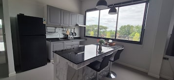 Uma cozinha moderna com bancada de mármore, eletrodomésticos pretos e uma janela ampla com vista para árvores e edifícios.