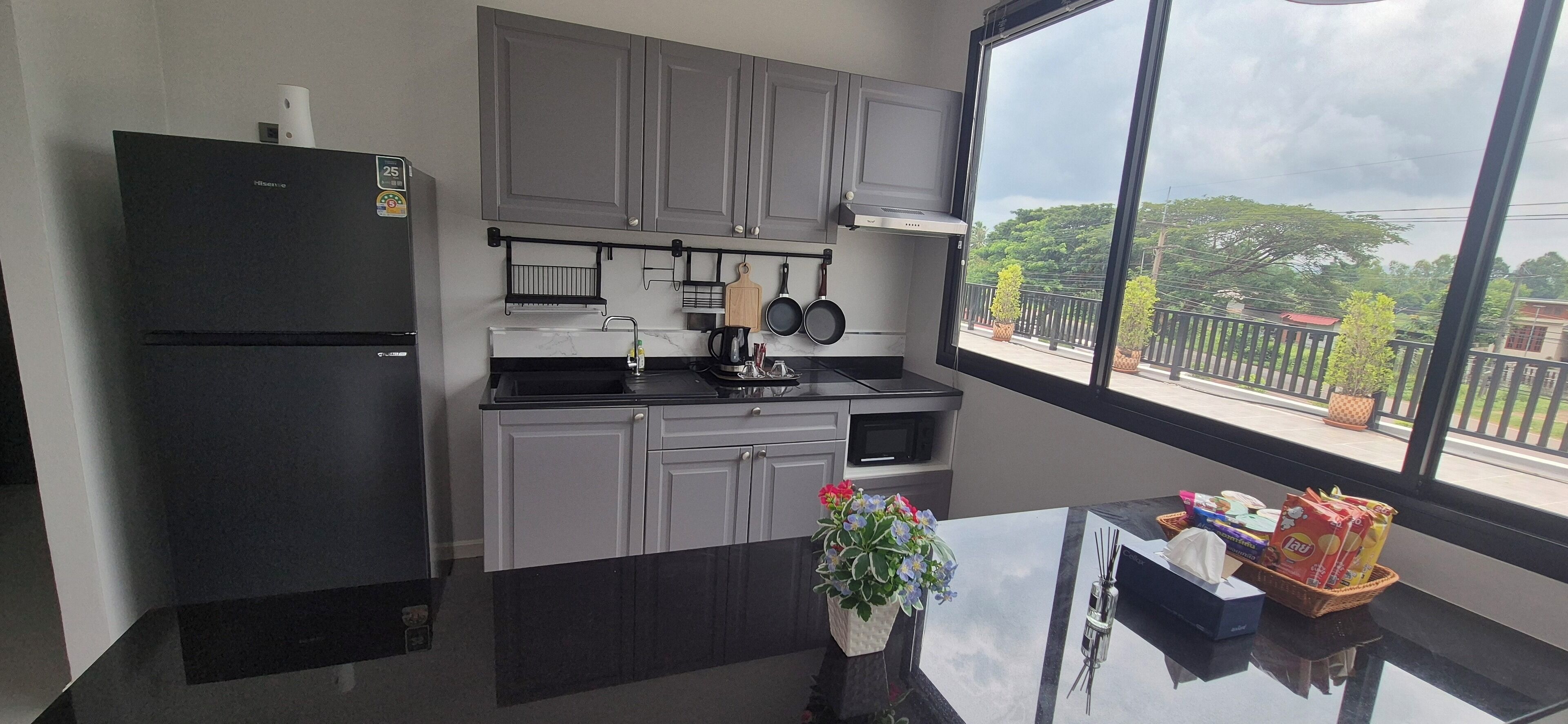 A modern kitchen with grey cabinets, a black refrigerator, and a window with a view of greenery and buildings.
