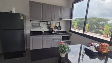 A modern kitchen with grey cabinets, a black refrigerator, and a window with a view of greenery and buildings.