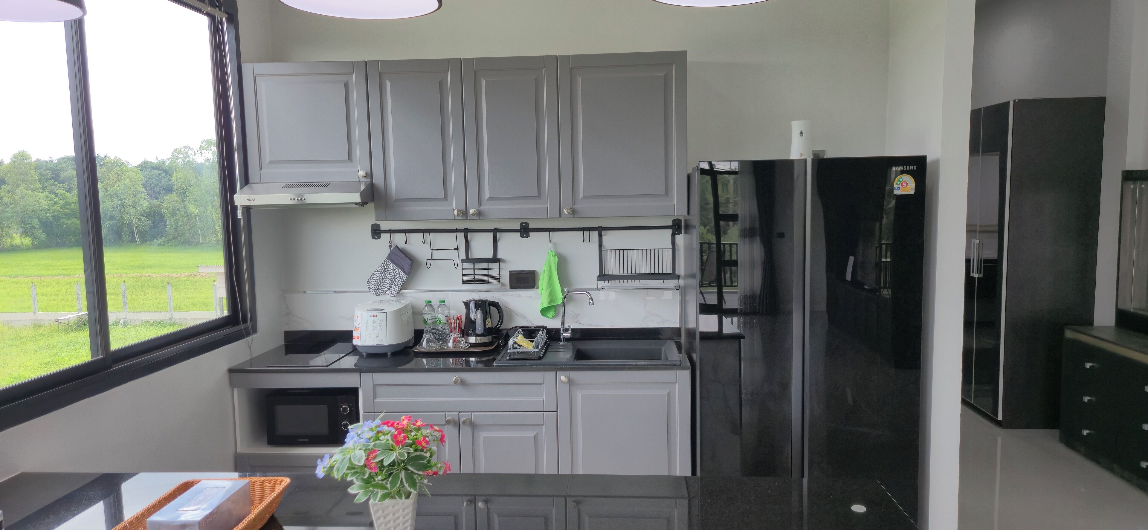 A modern kitchen with grey cabinets, a black refrigerator, and a window offering a view of a green field.