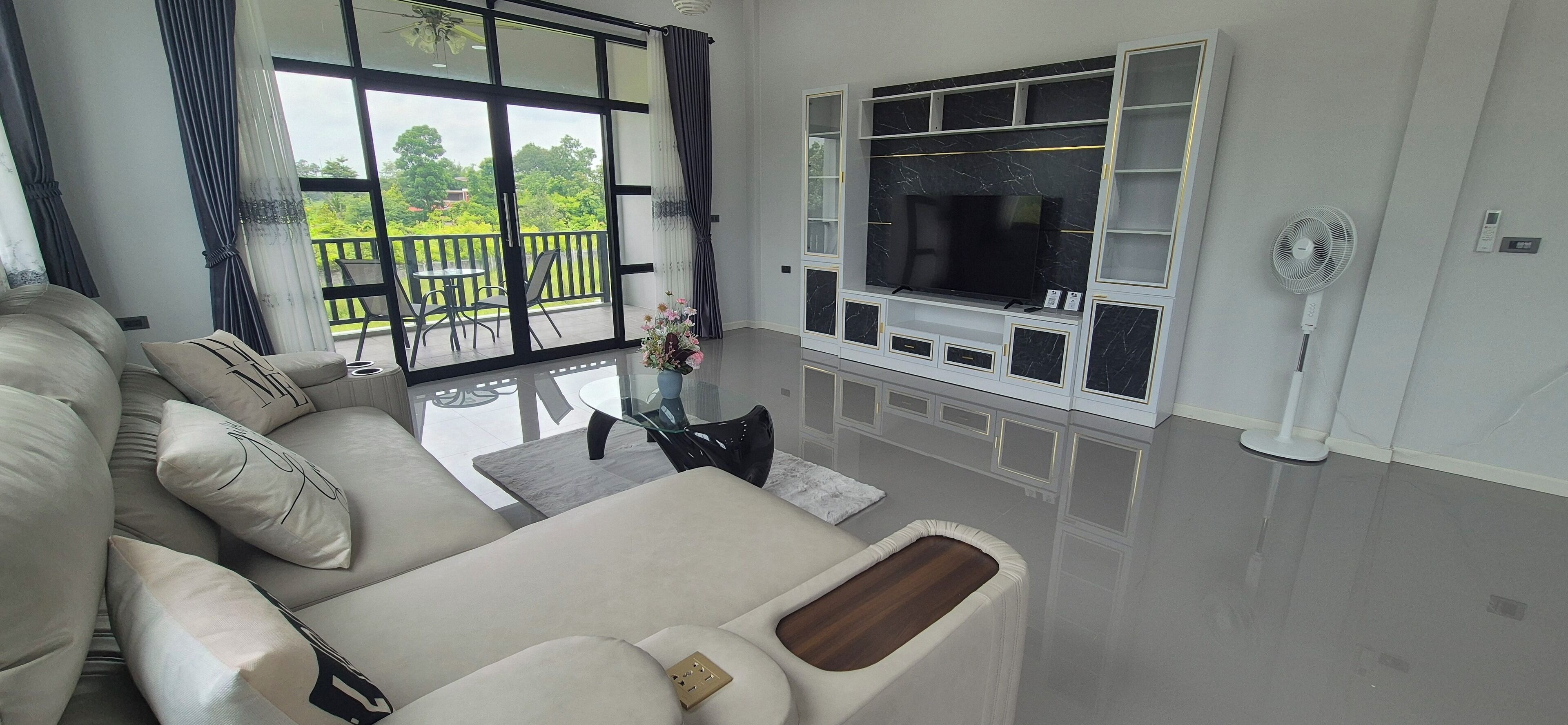 Una sala de estar moderna con un televisor grande, un sofá y un balcón con mobiliario exterior.
