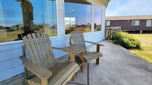 Deux fauteuils Adirondack en bois sont placés sur une terrasse en béton, à l’extérieur d’un bâtiment doté de grandes fenêtres.