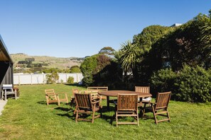 Un ensemble de mobilier de jardin en bois, comprenant des chaises et une table, entouré d’une végétation luxuriante et offrant une vue sur des collines en arrière-plan.