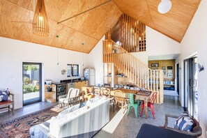 A spacious living area with a high ceiling, wooden beams, a dining table, and a staircase leading to an upper level.