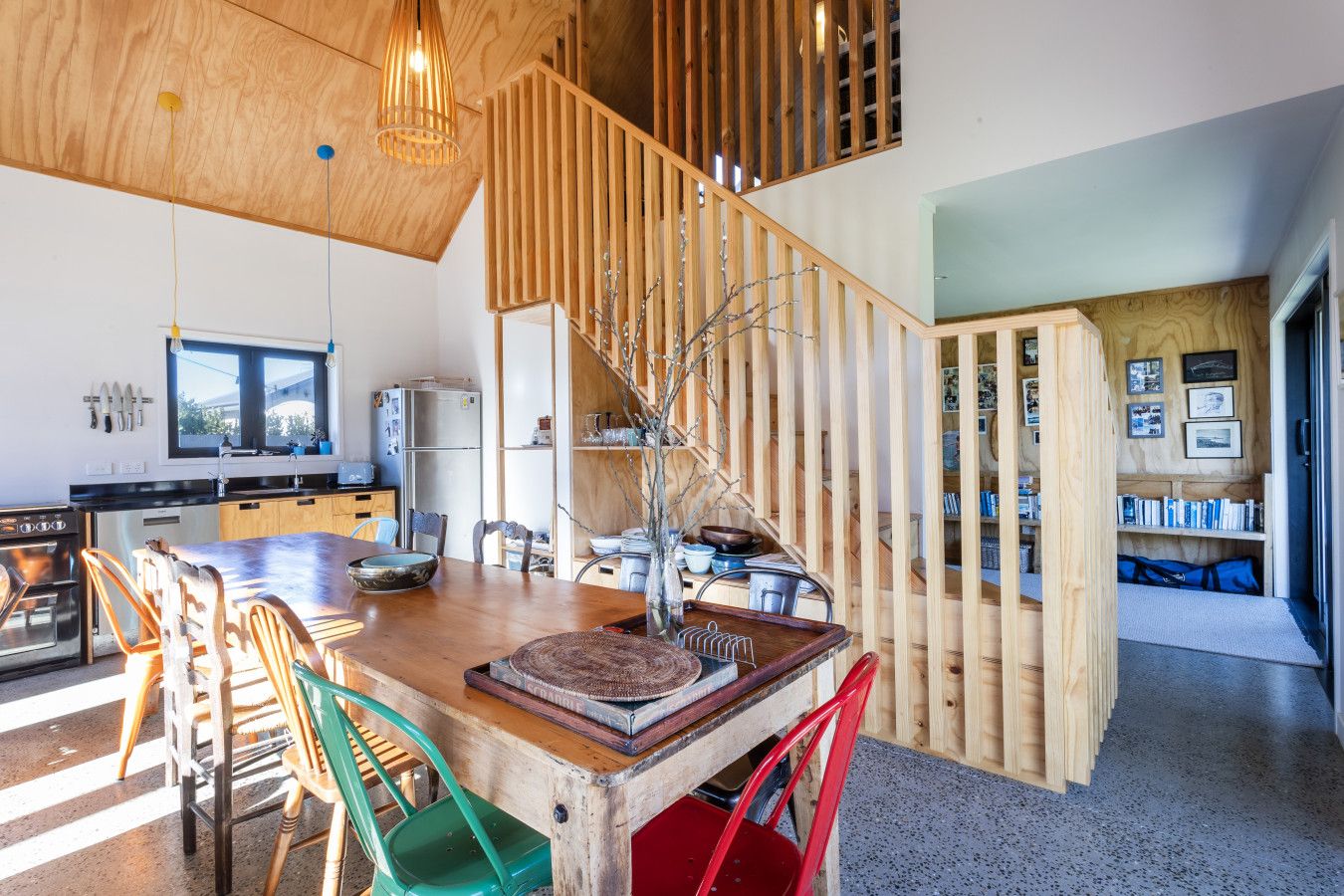 A modern kitchen with a wooden island, a dining area with mismatched chairs, and a staircase with a wooden railing.